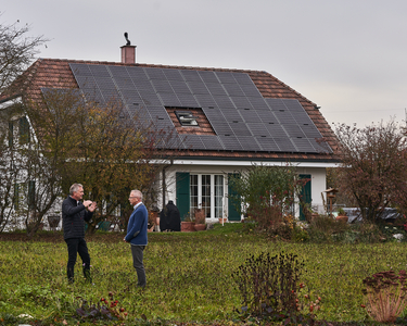 Einfamiilenhaus mit motnierter PV-Anlage auf der ganzen Dachbreite, vor dem Haus sind zwei Herren im Gespräch